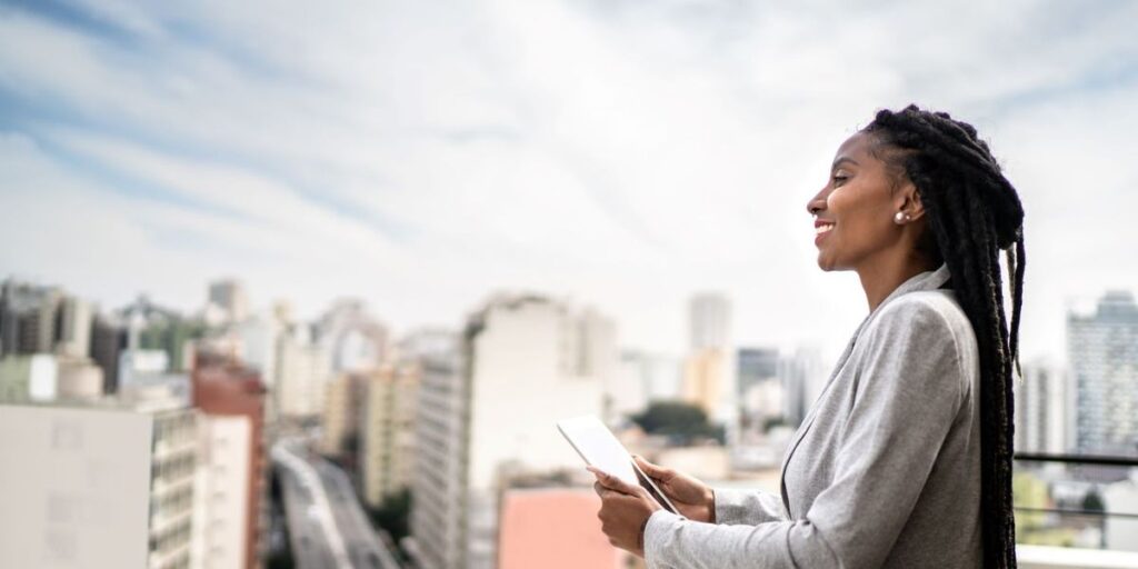 a-black-womaln-holding-an-ipad-looks-out-over-the-city-smiling.jpg
