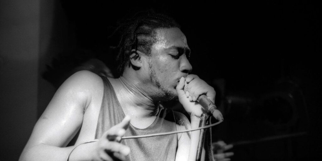 a-black-and-white-photo-of-ol-dirty-bastard-rapping-on-a-mic-with-a-tank-top-and-visible-sweat.jpg