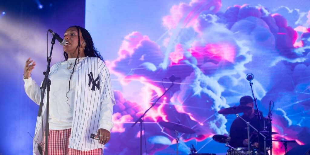 yaya-bey-wearing-a-new-york-baseball-jersy-performing-on-stage-in-front-a-psychadelic-screen-with-pink-and-blue-clouds.jpg