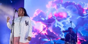 yaya-bey-wearing-a-new-york-baseball-jersy-performing-on-stage-in-front-a-psychadelic-screen-with-pink-and-blue-clouds.jpg