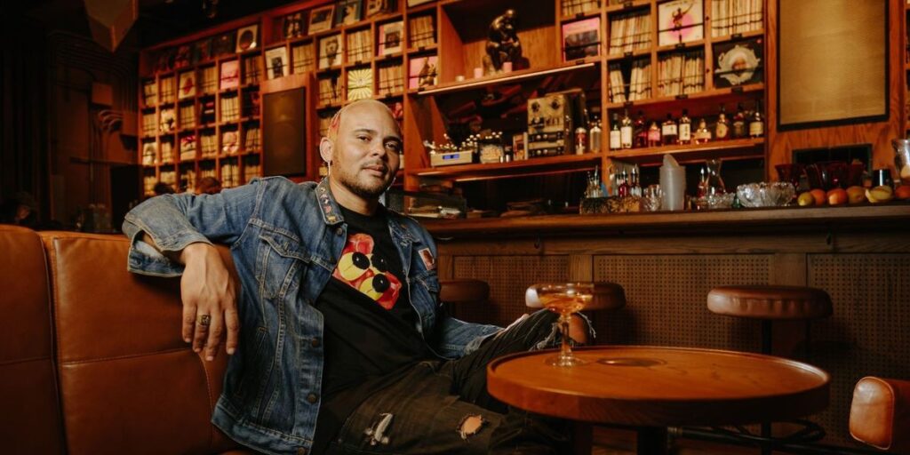 walshy-fire-sits-back-in-a-chair-at-an-upscale-bar-wearing-a-jean-jacket.jpg