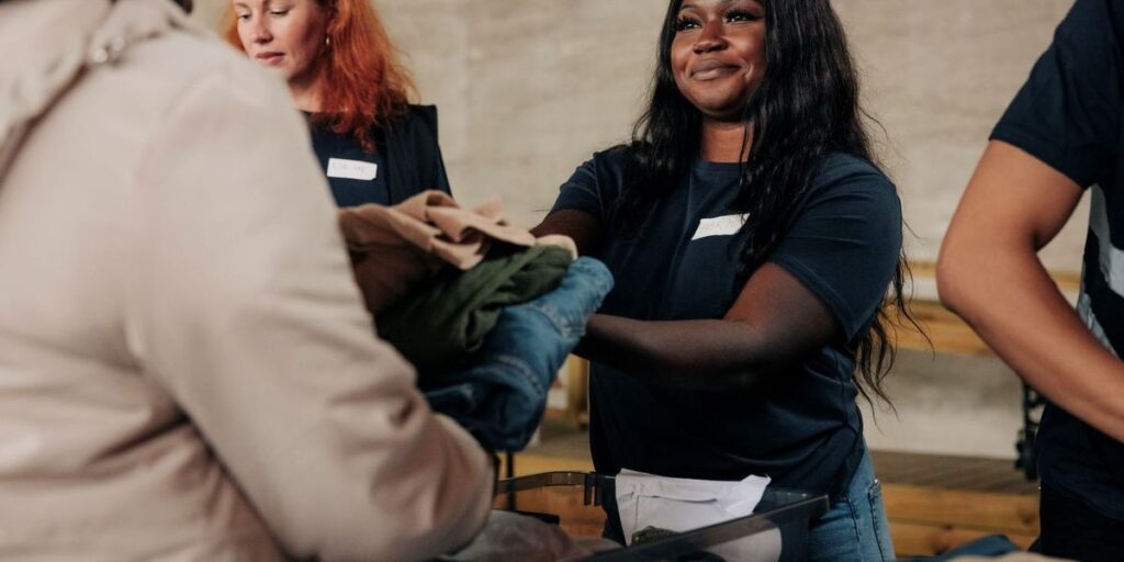 smiling-volunteer-giving-clothes-to-homeless-woman-at-community-center.jpg