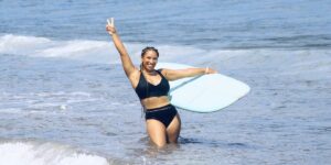 a-smiling-black-woman-holds-up-a-peace-sign-and-surfboard-in-the-water.jpg